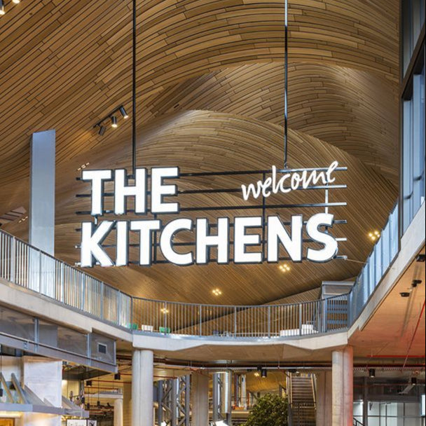 Large indoor space with 'The Kitchens' sign on a wooden ceiling